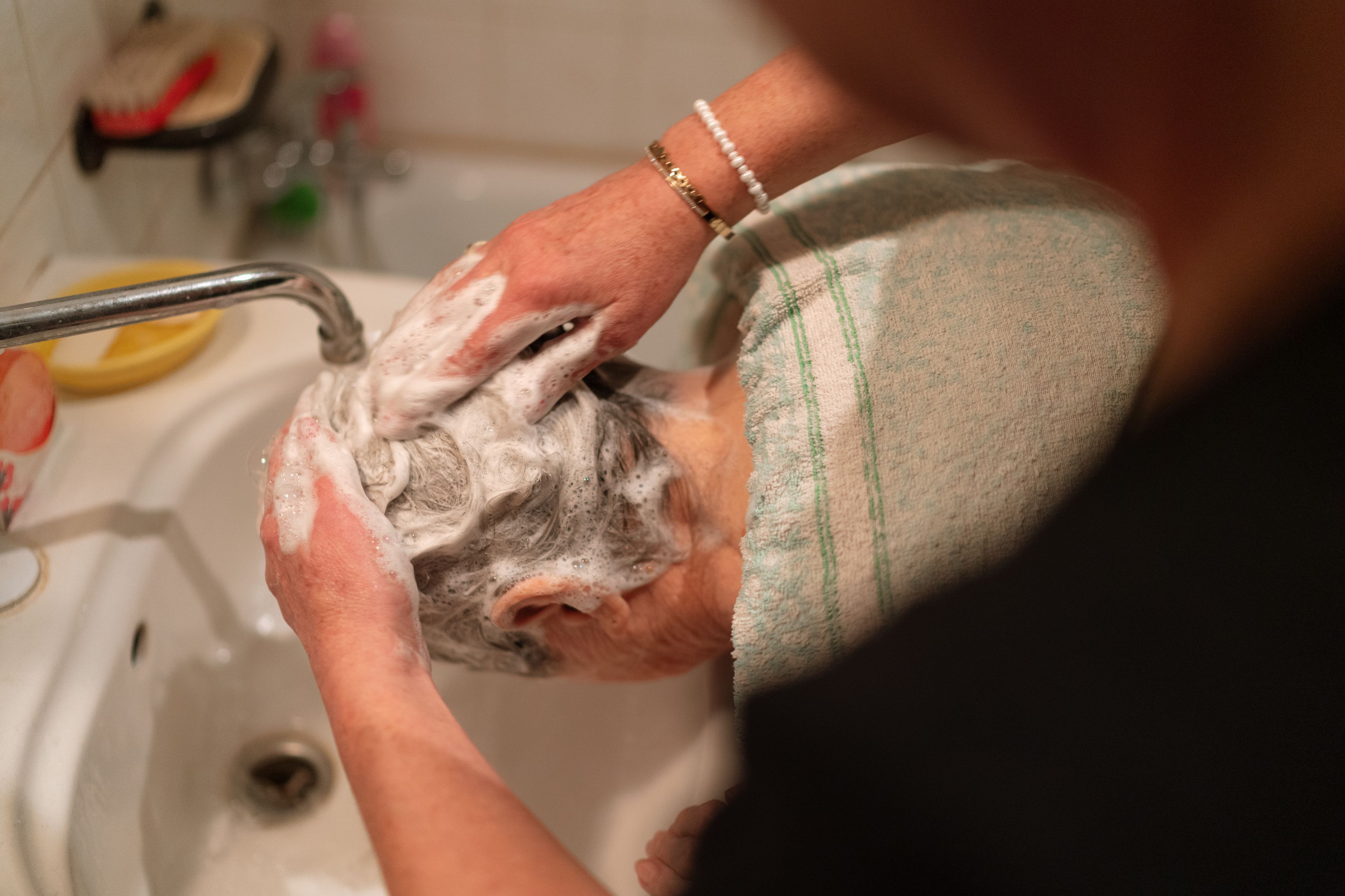 Pflegekraft wäscht behutsam die Haare einer älteren Person am Waschbecken
