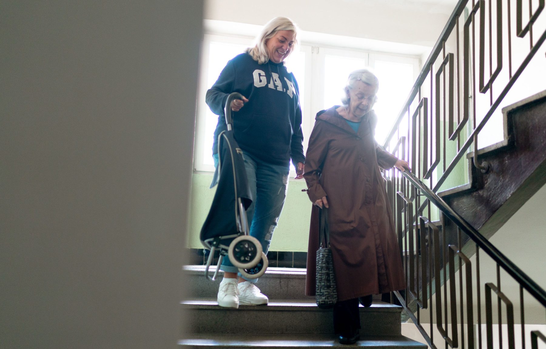 Pflegekraft begleitet eine aeltere Dame sicher die Treppe hinunter