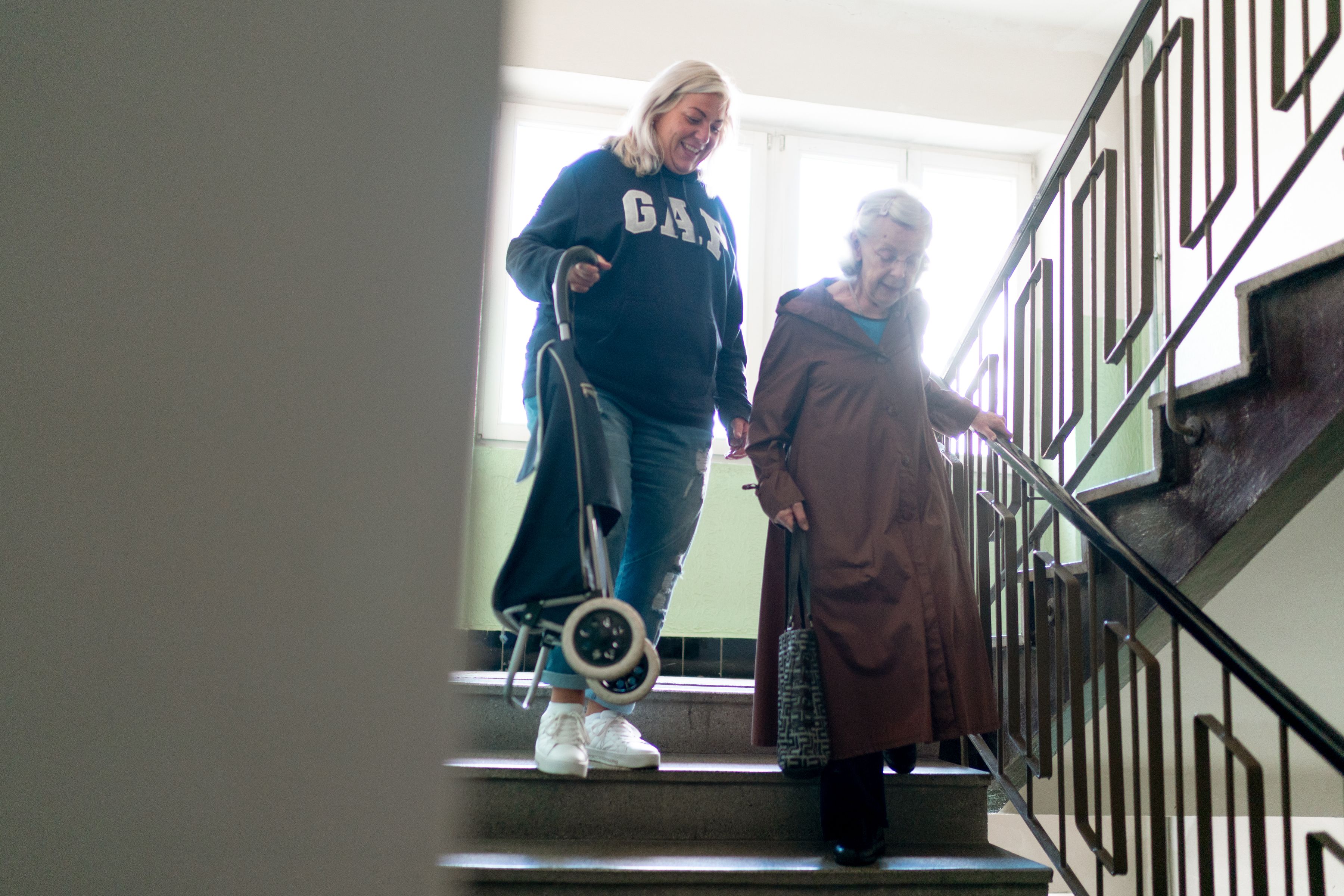 Pflegekraft begleitet eine ältere Dame sicher die Treppe hinunter
